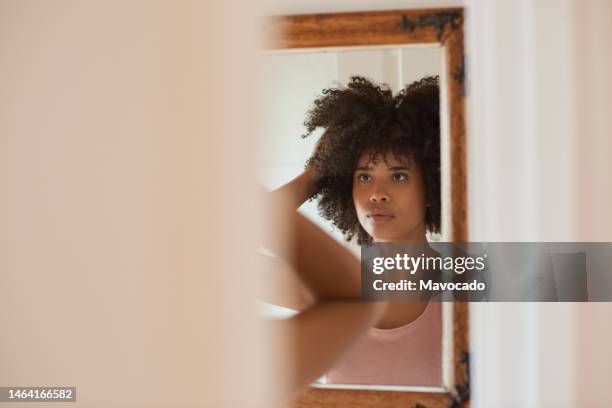 young african woman looking at her hair in a bathroom mirror - hand in hair stock pictures, royalty-free photos & images