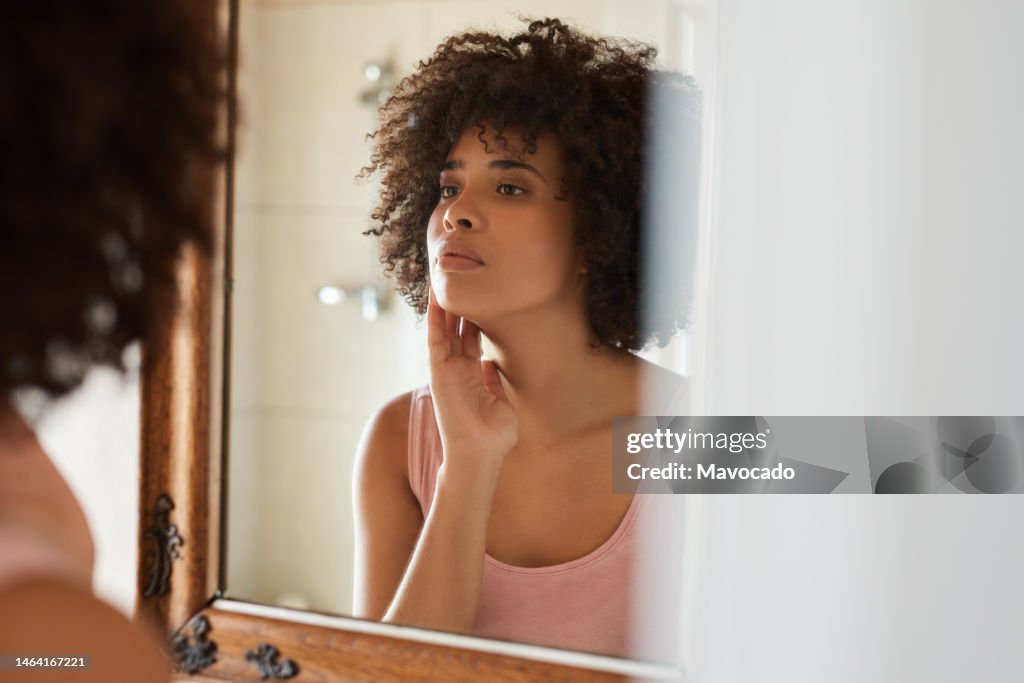 Young African woman examining her skin in a bathroom mirror