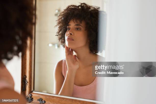 young african woman examining her skin in a bathroom mirror - frau gesicht beauty treatment stock-fotos und bilder
