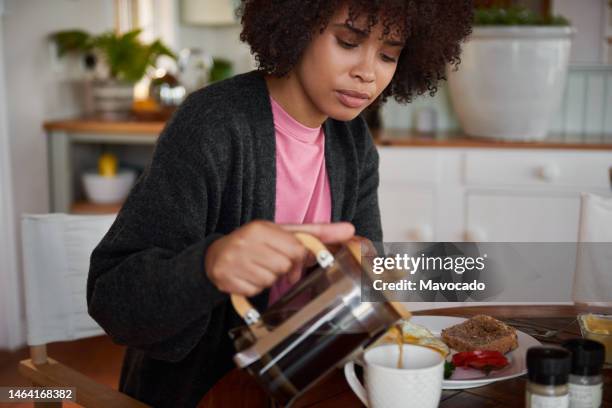 young african woman pouring a coffee while eating breakfast - simple living room stock pictures, royalty-free photos & images