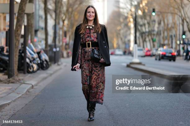 Alba Garavito Torre wears gold earrings, a gold large necklace with large pearls pendant, a black with burgundy / blue / beige flower print pattern...