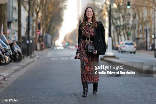 Alba Garavito Torre wears gold earrings, a gold large necklace with large pearls pendant, a black with burgundy / blue / beige flower print pattern...