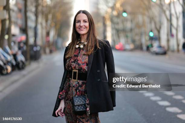 Alba Garavito Torre wears gold earrings, a gold large necklace with large pearls pendant, a black with burgundy / blue / beige flower print pattern...