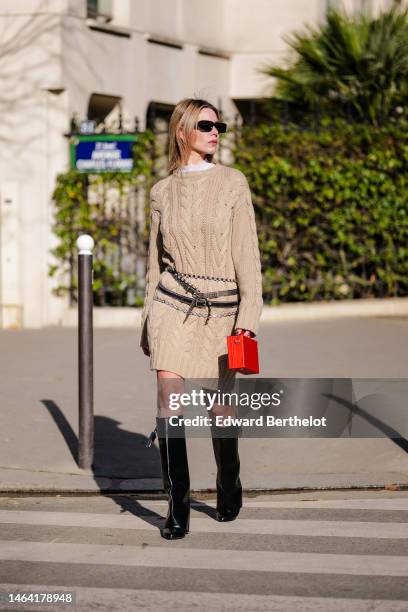 Natalia Verza wears black sunglasses, a white tulle high neck from Givenchy, a beige braided wool pullover, a red shiny leather malle handbag from...