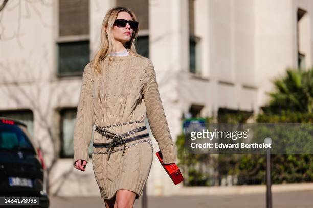Natalia Verza wears black sunglasses, a white tulle high neck from Givenchy, a beige braided wool pullover, a red shiny leather malle handbag from...