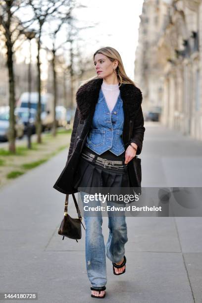 Natalia Verza wears silver earrings, a white tulle high neck t-shirt from Givenchy, a blue denim buttoned / gilet, a black shiny leather with black...