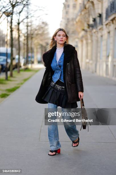 Natalia Verza wears silver earrings, a white tulle high neck t-shirt from Givenchy, a blue denim buttoned / gilet, a black shiny leather with black...