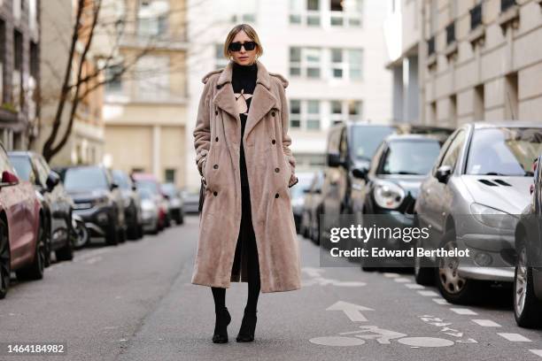 Emy Venturini wears black sunglasses, gold earrings, a black turtleneck / cut-out chest dress from Amazuin, a beige fluffy long coat from Burberry,...