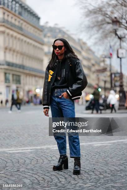 Emilie Joseph wears black sunglasses, a black hoodie sweater from Ami, a black felt and leather sleeves with embroidered yellow yoke oversized teddy...