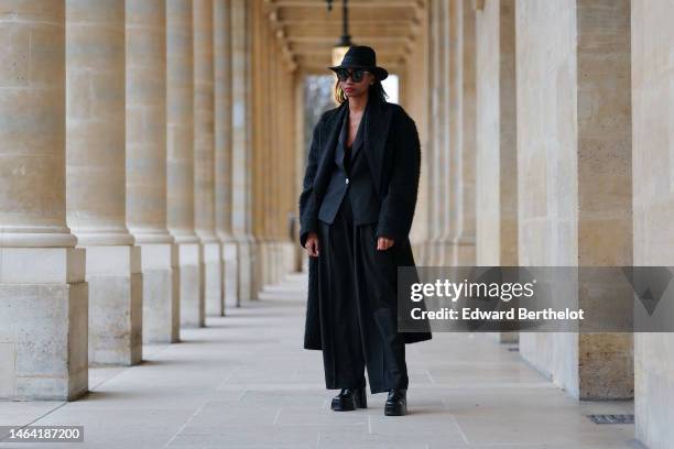 Emilie Joseph wears a black felt wool hat, black sunglasses, a black V-neck silk tank-top, a black blazer jacket from Balmain, a black long wool...