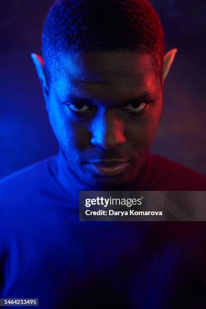 a black man in blue and red with elf ears and neon light. art portrait of a man on a dark background with  copy space. - low key imagens e fotografias de stock