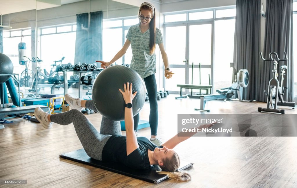Rehabilitation specialist instructing a woman exercising with a fitness ball at the gym