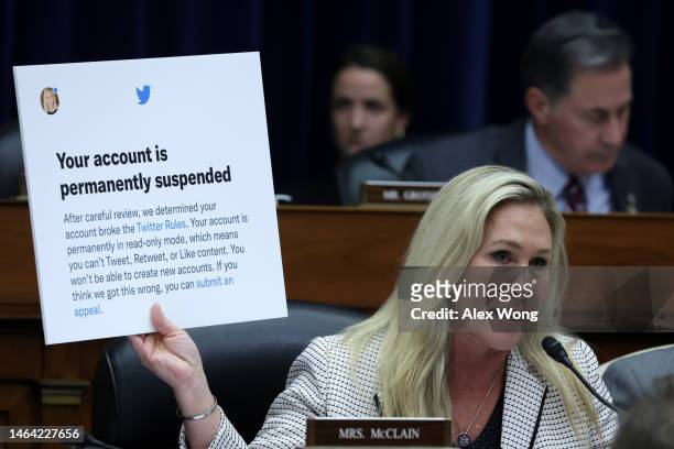 Rep. Marjorie Taylor-Greene holds up a poster of a Twitter announcement of suspending her account during a hearing before the House Oversight and...