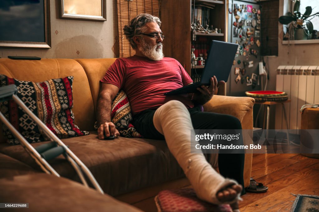 Reifer Mann mit gebrochenem Bein im Gipsverband auf dem Sofa