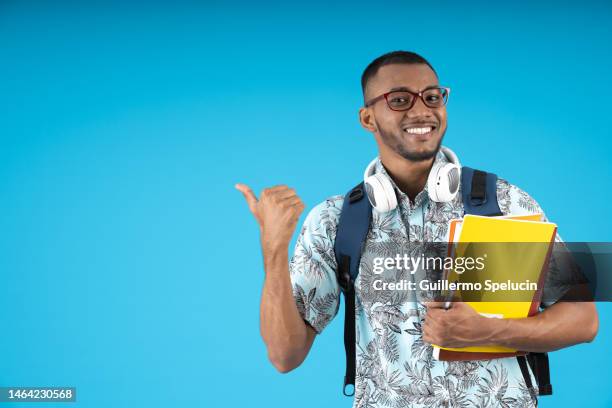 young african american male student with glasses, posing smiling, pointing with thumb and his notebooks - headphone man on neck stockfoto's en -beelden