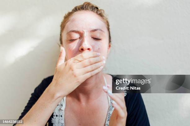 portrait of the face of a happy young caucasian blonde woman applying sunscreen - parasols stockfoto's en -beelden