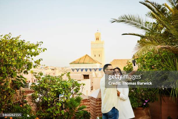 medium shot of couple taking selfie from rooftop of hotel in marrakech - premium access images stock pictures, royalty-free photos & images