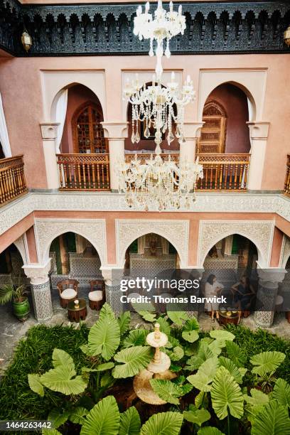 extreme wide shot of friends relaxing in courtyard of luxury hotel - legs crossed at knee stock pictures, royalty-free photos & images