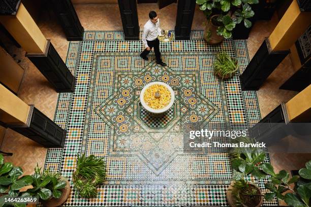 wide shot of waiter carrying  tea service through courtyard in hotel - fountain courtyard fotografías e imágenes de stock