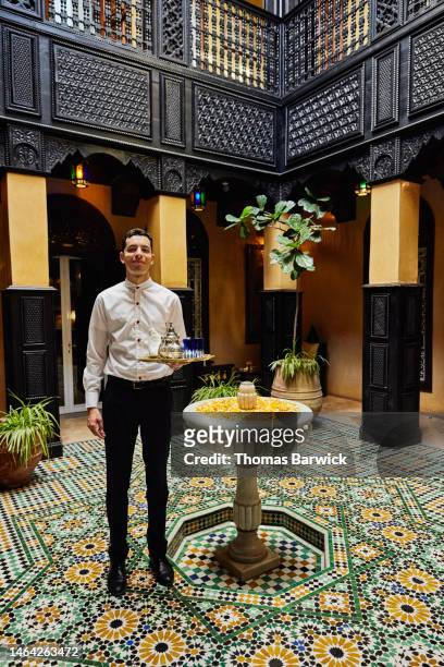 Wide shot of waiter holding tea service in courtyard of luxury hotel