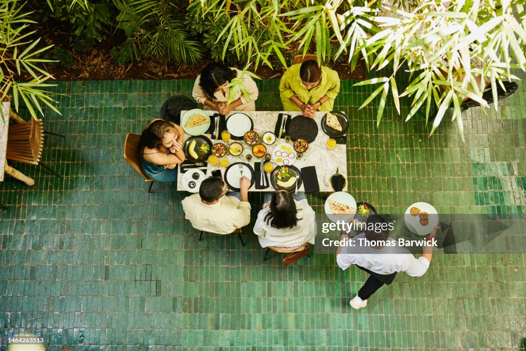 Wide shot of waiter bringing food to table of friends in restaurant