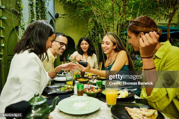 medium shot of friends looking at smart phone while sharing lunch - outdoor dining stock pictures, royalty-free photos & images