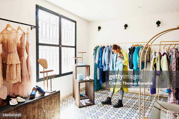 wide shot of woman admiring coat while shopping in clothing boutique - blue coat stock-fotos und bilder