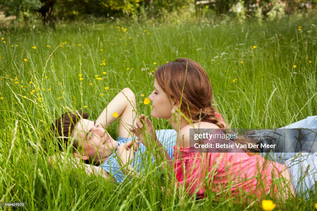 Couple laying in grass, woman smelling flower.