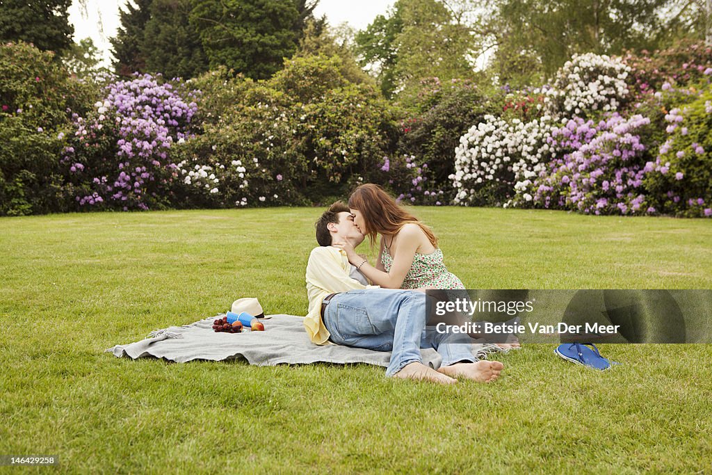 Couple kissing, having picnic in park.