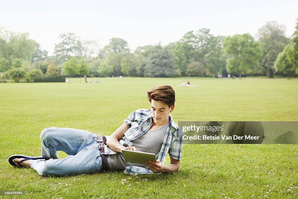 Man relaxing in grass,using tablet computer.