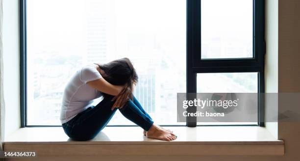 sad woman sitting on window sill - casual woman pensive side view stockfoto's en -beelden