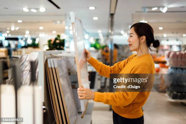 beautiful young asian woman shopping for home decor and household necessities, choosing for picture frames in a homeware store - accessory stockfoto's en -beelden
