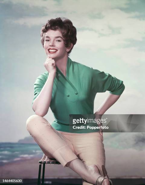 Posed studio portrait of English actress Dawn Addams wearing a green top with a shawl neck and cream capri pants in London, 16th March 1957.