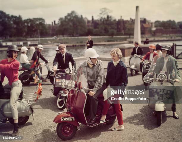 Men and women from a scooter club posed on their Vespa scooters beside Hampton Court Bridge and the River Thames at East Molesey in Surrey, England...