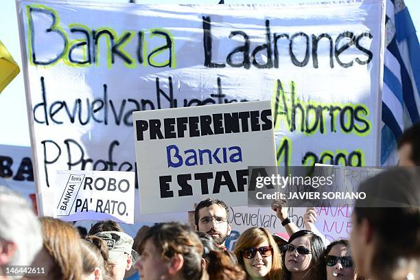 People hold placards reading "Bankia, thieves, gives us our savings back" and "Bankia fraud" during a demonstration on June 16, 2012 in Madrid....