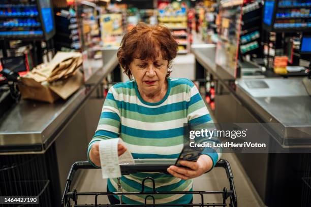 ältere frau prüft rechnung nach dem einkauf im supermarkt - shopping cart stock-fotos und bilder