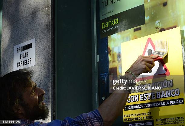 Man sticks a placard reading "Caution with this bank" on the windowcase of a Spanish bank Bankia office during a demonstration against bank fraud on...