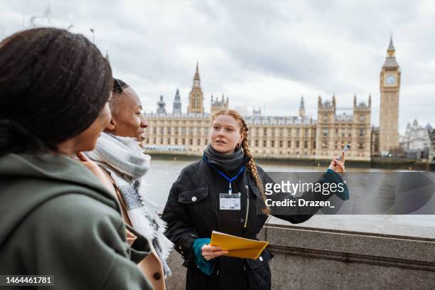 young tourists in london, followed by private tour guide, showing them parliament and big ben - gids stockfoto's en -beelden