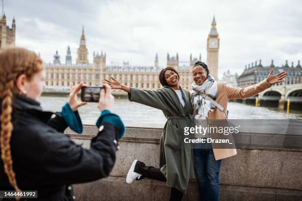 young african couple are tourist in london, in wintertime. redhead woman taking pictures with smart phone - couple traveling stock pictures, royalty-free photos & images