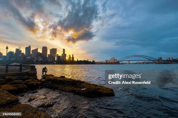 Person standing on rocks takes photos of The Sydney Opera House and Harbour Bridge during sunset at Mrs Macquaries Point on February 09, 2023 in...