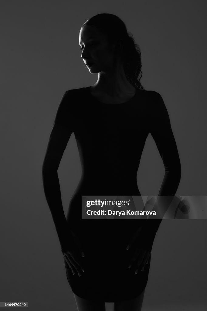 A beautiful young woman is in the shadow. A portrait with a light on the face with copy space. The profile of woman from behind with beautiful figure.