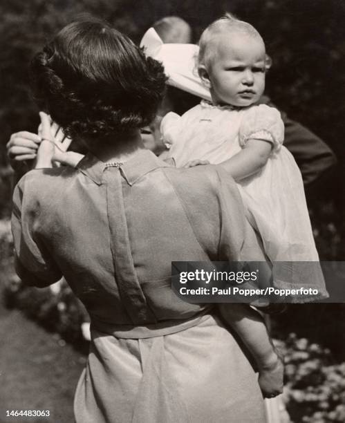 British Royal Queen Elizabeth II with her back to the camera, carrying her daughter, Princess Anne of Edinburgh, in the grounds of Clarence House,...