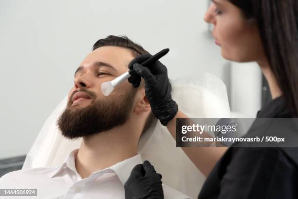 young bearded man getting laser facial treatment by professional - laser face stock pictures, royalty-free photos & images