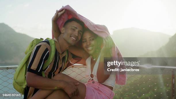 romantic summer. african ethnicity couple together on vacations watching the lovely view of mountains. hiding from rain under jacket - hot wives photos stock pictures, royalty-free photos & images