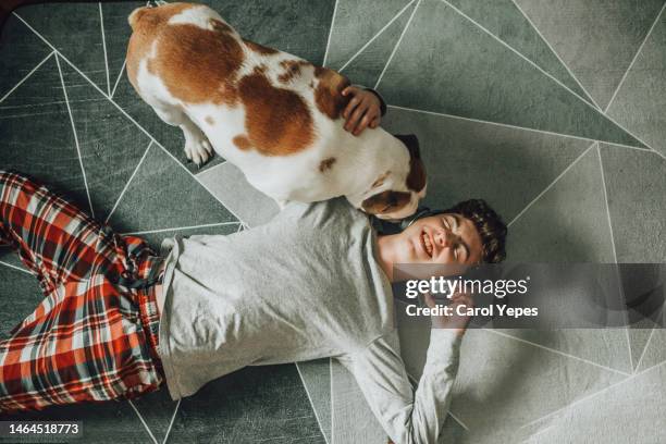 boy listening music with headphones lying on carpet with playful dog around - boy singing stock-fotos und bilder