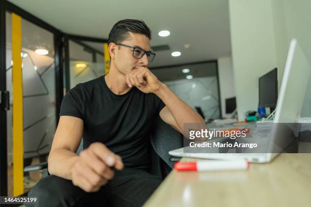 latino man is inside the office of the company he works for, with a laptop organizing pending work - pending stock pictures, royalty-free photos & images
