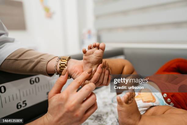 pediatra joven sostiene el pie de un bebé recién nacido - pie humano fotografías e imágenes de stock