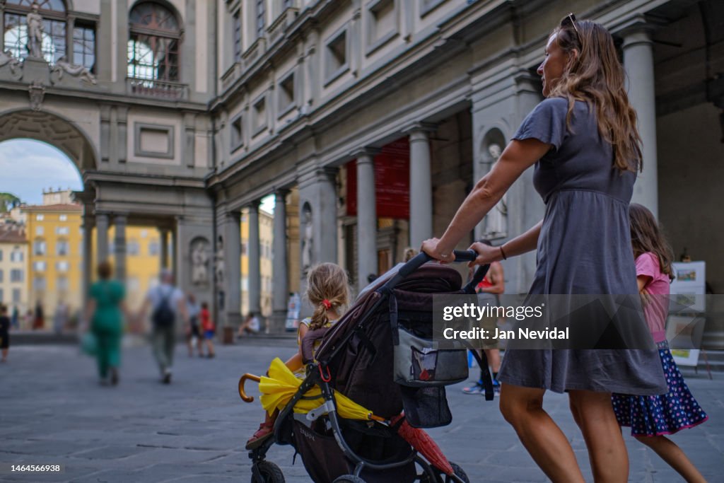Young family with children and a stroller walking down the street in Florence in front of Uffizi gallery