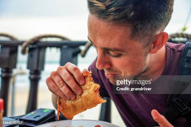 young man in his twenties sitting at a beach-side open air restaurant eating a delicious shrimp taco in tijuana mexico - ensenada stock pictures, royalty-free photos & images