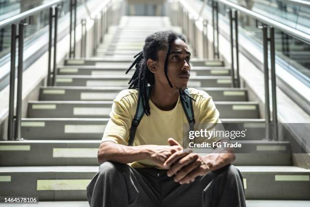 joven contemplativo sentado en las escaleras de la estación de metro - mirar alrededor fotografías e imágenes de stock